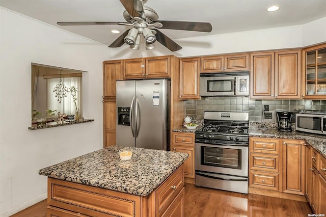 kitchen featuring decorative backsplash, appliances with stainless steel finishes, ceiling fan with notable chandelier, dark stone countertops, and dark hardwood / wood-style floors