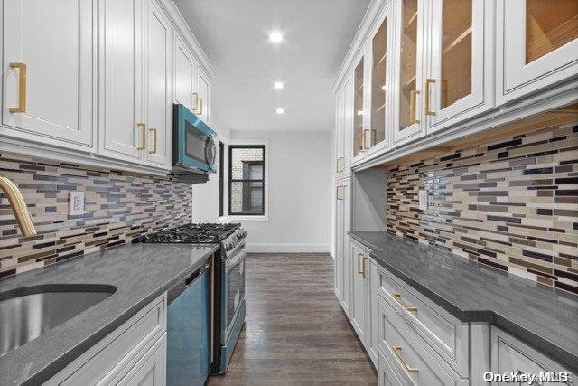 kitchen with backsplash, dark stone counters, dark hardwood / wood-style flooring, white cabinetry, and stainless steel appliances