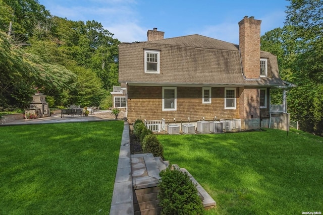 rear view of property featuring a fireplace, a patio, cooling unit, and a lawn