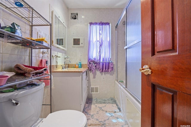 full bathroom with vanity, bath / shower combo with glass door, tile walls, and toilet