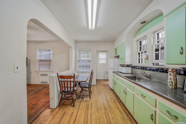 kitchen with green cabinetry, white appliances, sink, and light hardwood / wood-style flooring