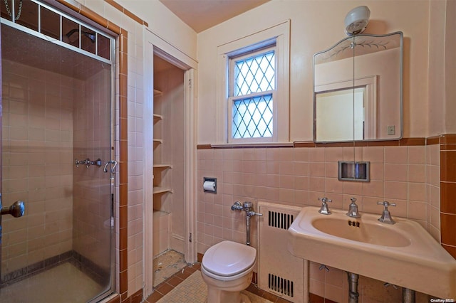 bathroom featuring tile patterned floors, radiator, a shower with door, tile walls, and toilet