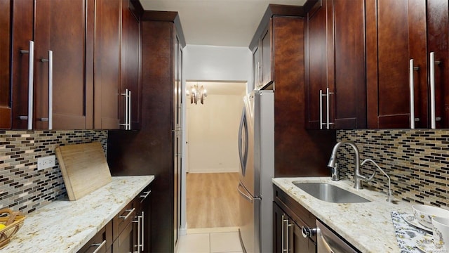 kitchen featuring decorative backsplash, light stone countertops, sink, and stainless steel refrigerator