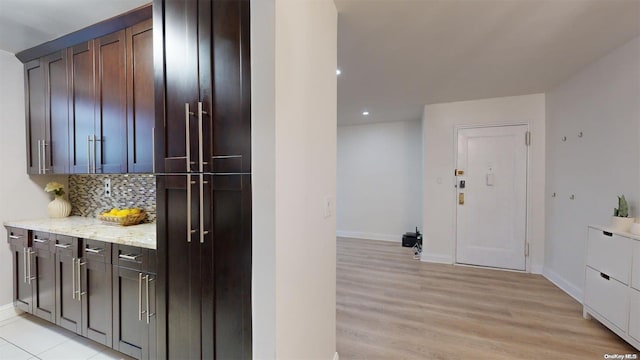 kitchen with light stone counters, light wood-type flooring, backsplash, and dark brown cabinetry