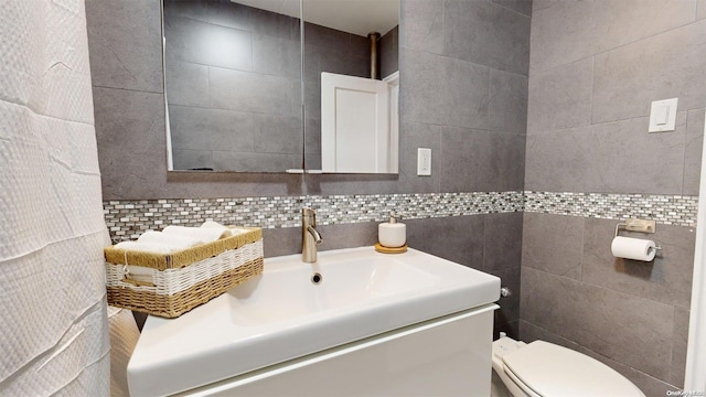 bathroom featuring vanity, toilet, decorative backsplash, and tile walls