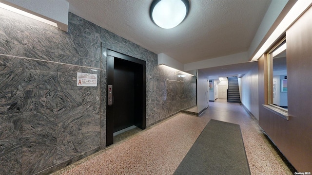 hallway featuring a textured ceiling, elevator, and tile walls