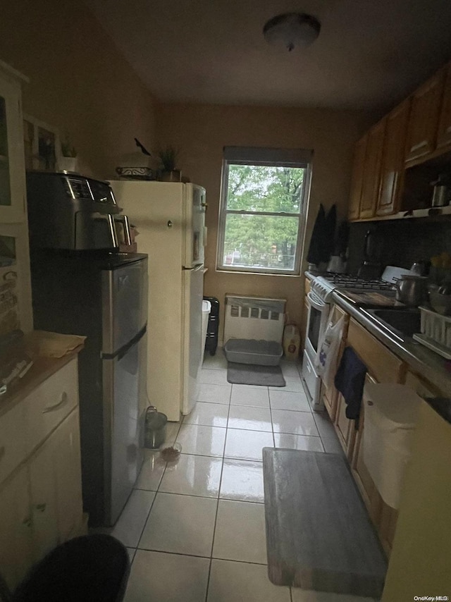 kitchen featuring sink, white appliances, radiator, and light tile patterned flooring