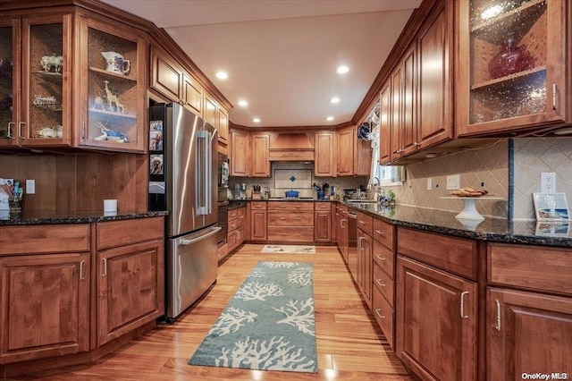 kitchen with dark stone countertops, light wood-type flooring, premium range hood, and appliances with stainless steel finishes