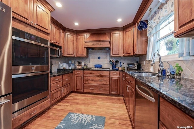 kitchen with appliances with stainless steel finishes, tasteful backsplash, custom exhaust hood, sink, and light hardwood / wood-style floors