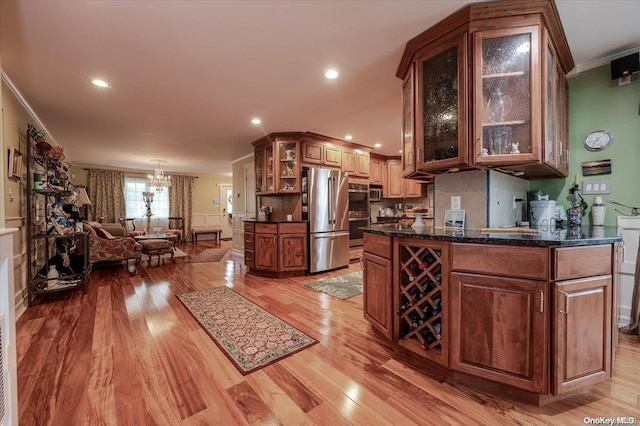 kitchen with appliances with stainless steel finishes, tasteful backsplash, ornamental molding, a notable chandelier, and light hardwood / wood-style floors