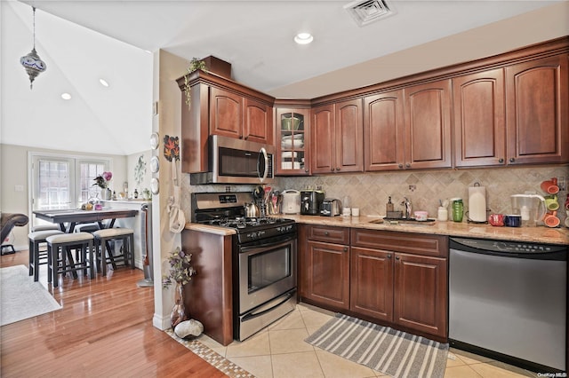 kitchen featuring backsplash, sink, vaulted ceiling, light wood-type flooring, and appliances with stainless steel finishes