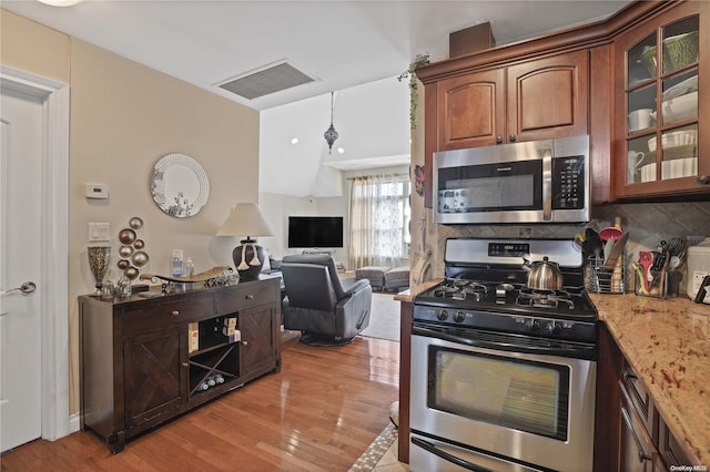 kitchen with backsplash, light stone countertops, light hardwood / wood-style flooring, and appliances with stainless steel finishes