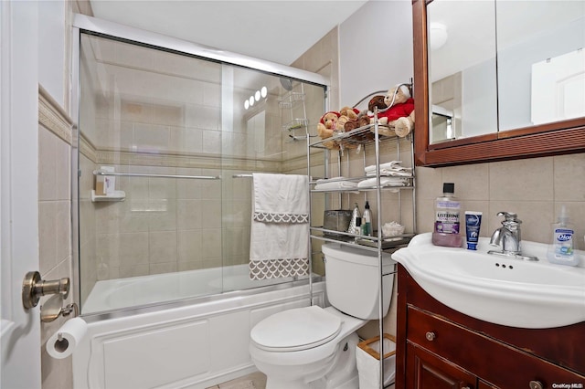 full bathroom featuring combined bath / shower with glass door, tasteful backsplash, vanity, tile walls, and toilet