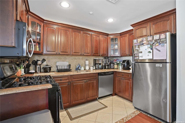 kitchen with appliances with stainless steel finishes, tasteful backsplash, light stone counters, sink, and light tile patterned floors