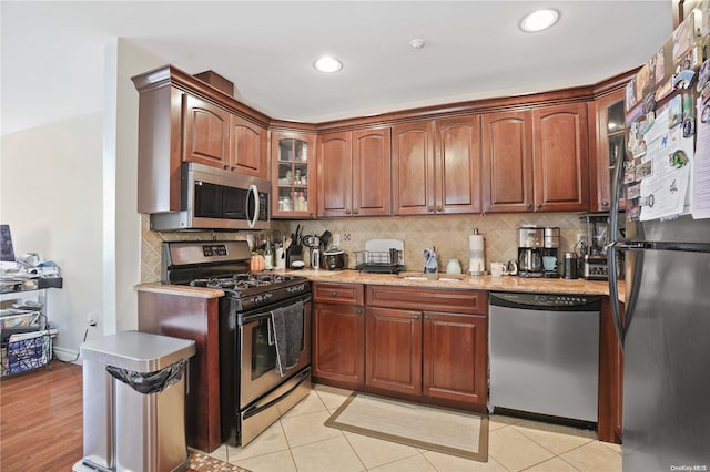 kitchen with sink, light stone counters, decorative backsplash, light tile patterned flooring, and appliances with stainless steel finishes