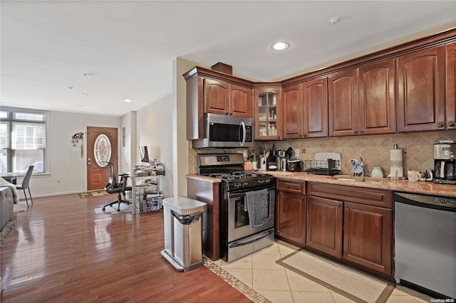 kitchen featuring appliances with stainless steel finishes, backsplash, light stone counters, sink, and light hardwood / wood-style floors