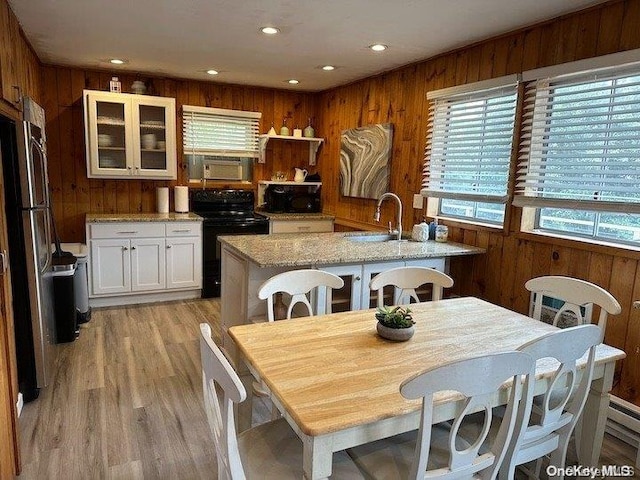 kitchen featuring sink, white cabinetry, wood walls, black range with electric stovetop, and an island with sink