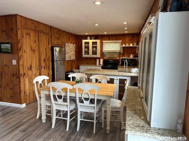 kitchen with wooden walls, dark hardwood / wood-style floors, gas stove, light stone counters, and stainless steel refrigerator