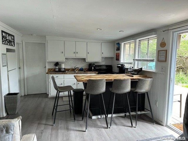 kitchen featuring sink, butcher block countertops, light hardwood / wood-style floors, white cabinetry, and a breakfast bar area