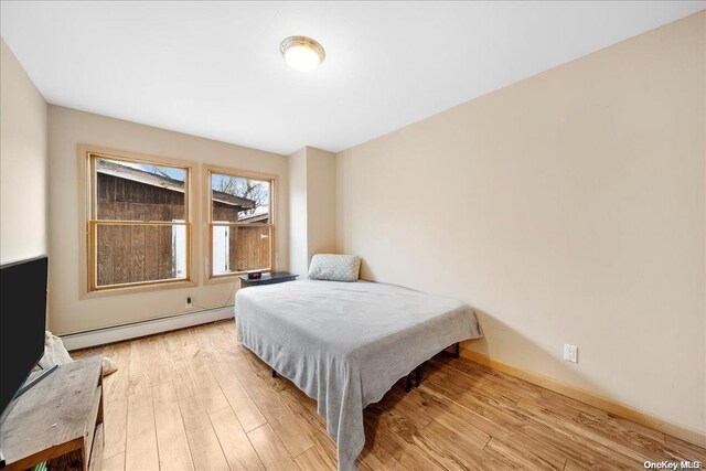 bedroom with light wood-type flooring and a baseboard heating unit