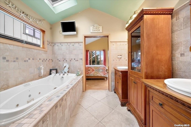 bathroom with tile patterned floors, tiled tub, vaulted ceiling with skylight, vanity, and tile walls