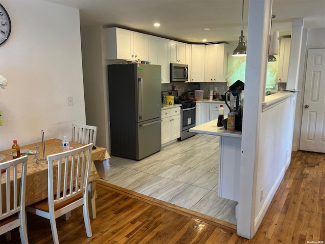 kitchen with hanging light fixtures, stainless steel appliances, light hardwood / wood-style flooring, and white cabinetry