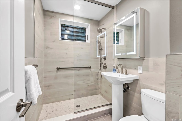 bathroom with sink, tiled shower, toilet, and tile walls