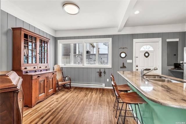 kitchen with beam ceiling, sink, a baseboard heating unit, light hardwood / wood-style floors, and a breakfast bar