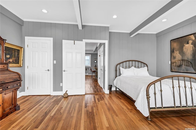 bedroom with beamed ceiling, hardwood / wood-style flooring, ornamental molding, and wood walls