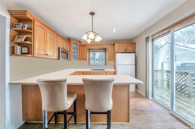 kitchen with a kitchen breakfast bar, hanging light fixtures, white fridge, kitchen peninsula, and light hardwood / wood-style flooring