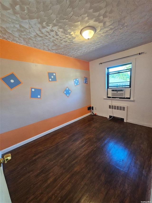 spare room with a textured ceiling, dark hardwood / wood-style floors, radiator, and cooling unit