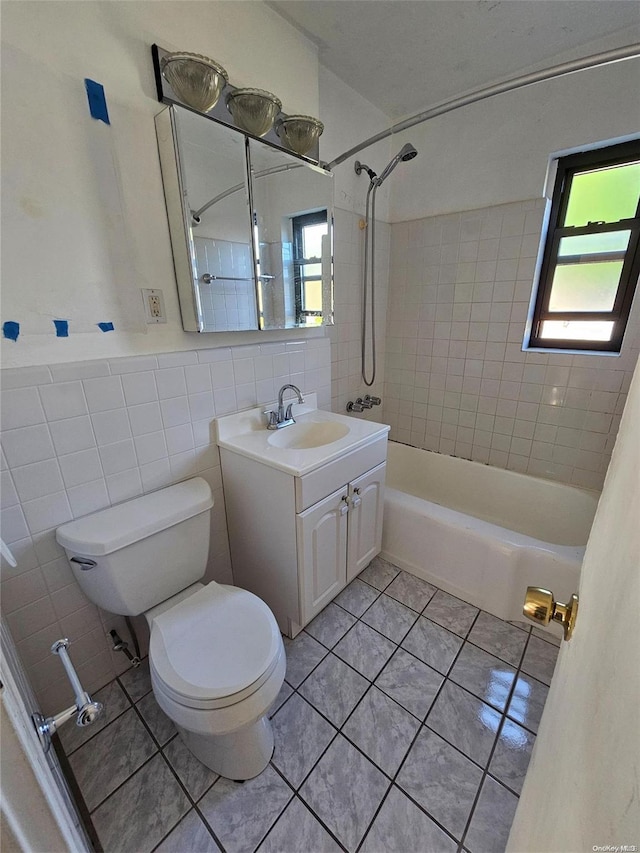 full bathroom with vanity, tile patterned floors, tiled shower / bath, toilet, and tile walls