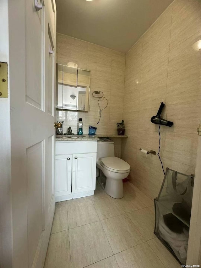 bathroom with tile patterned flooring, vanity, toilet, and tile walls