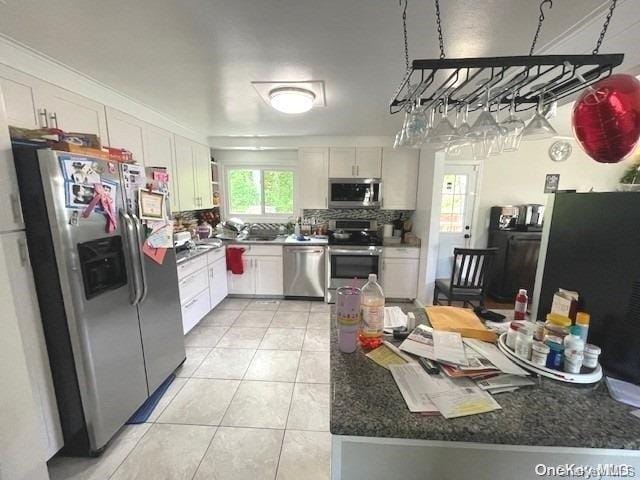 kitchen featuring stainless steel appliances, white cabinets, dark stone counters, decorative backsplash, and light tile patterned flooring