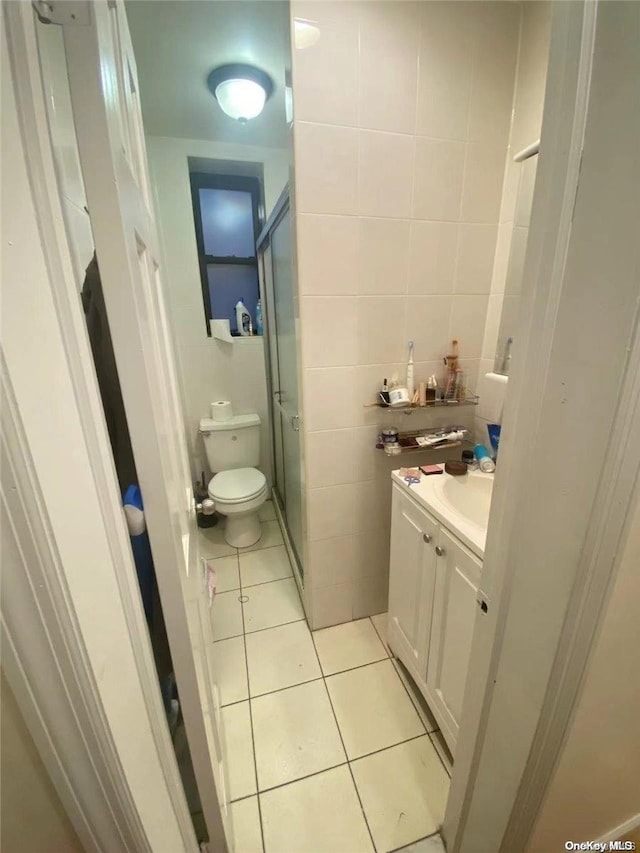 bathroom with vanity, a shower with door, tile patterned flooring, toilet, and tile walls