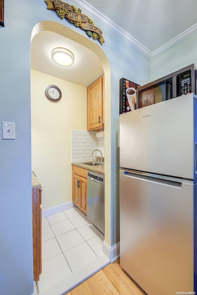 kitchen with backsplash, ornamental molding, stainless steel appliances, sink, and light hardwood / wood-style flooring