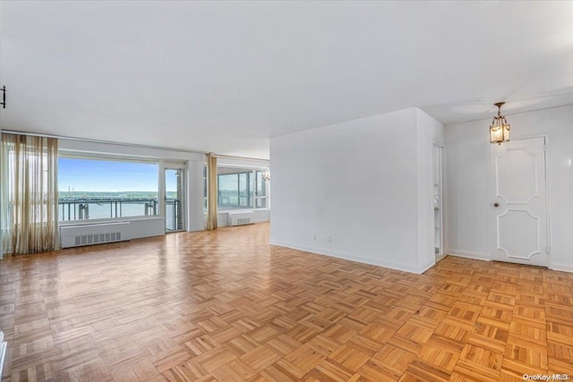 unfurnished living room with a chandelier, radiator heating unit, a water view, and light parquet floors