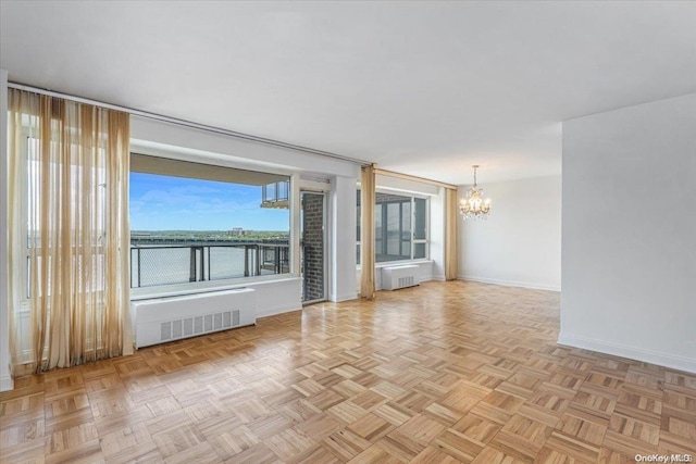 empty room featuring radiator, a wealth of natural light, a water view, and a notable chandelier