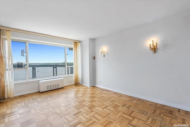 unfurnished room featuring a water view, radiator heating unit, and light parquet flooring