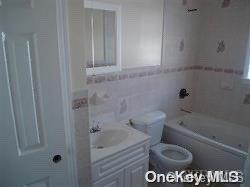 bathroom featuring a tub to relax in, vanity, tile walls, and toilet