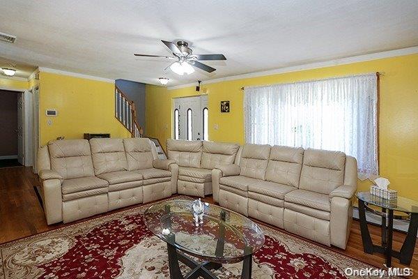 living room featuring wood-type flooring, baseboard heating, ceiling fan, and ornamental molding