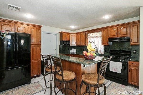 kitchen featuring a kitchen island, a breakfast bar area, decorative backsplash, light tile patterned floors, and black appliances