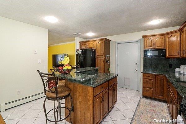 kitchen with a center island, backsplash, black appliances, light tile patterned floors, and baseboard heating