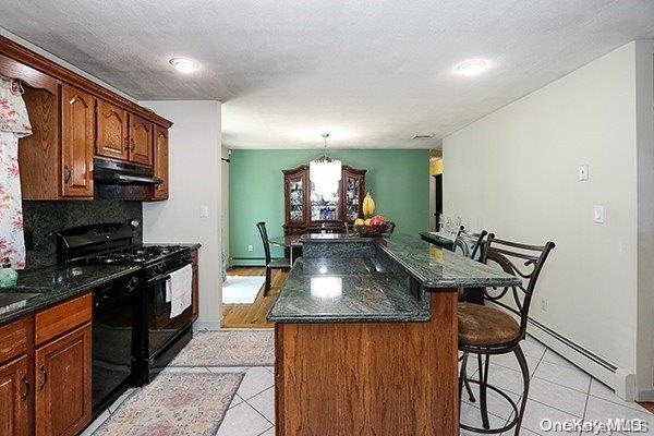 kitchen featuring a center island, black appliances, light tile patterned floors, baseboard heating, and a kitchen bar