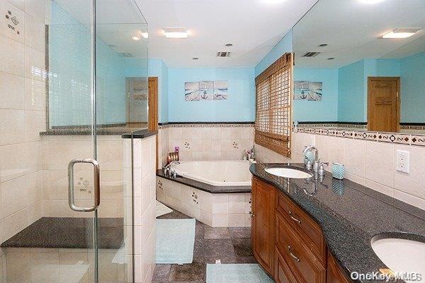 bathroom with tile patterned floors, vanity, shower with separate bathtub, and tile walls