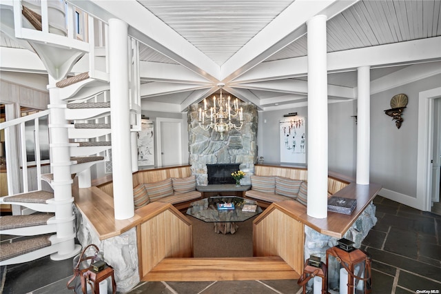 living room with a notable chandelier, beam ceiling, and a stone fireplace