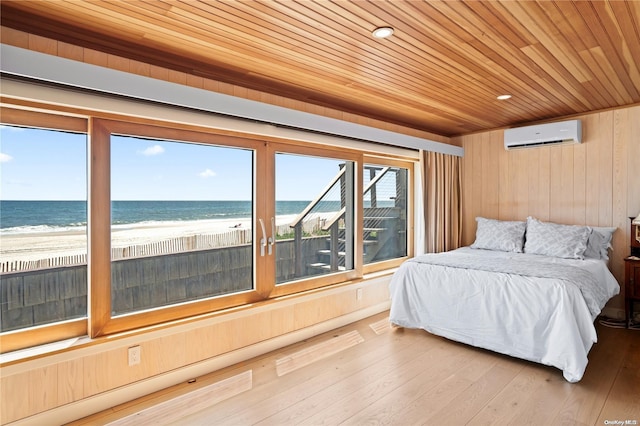 bedroom featuring hardwood / wood-style floors, wood walls, a view of the beach, and a water view