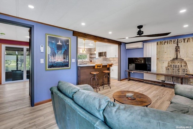 living room featuring ceiling fan, a wall unit AC, and light hardwood / wood-style flooring