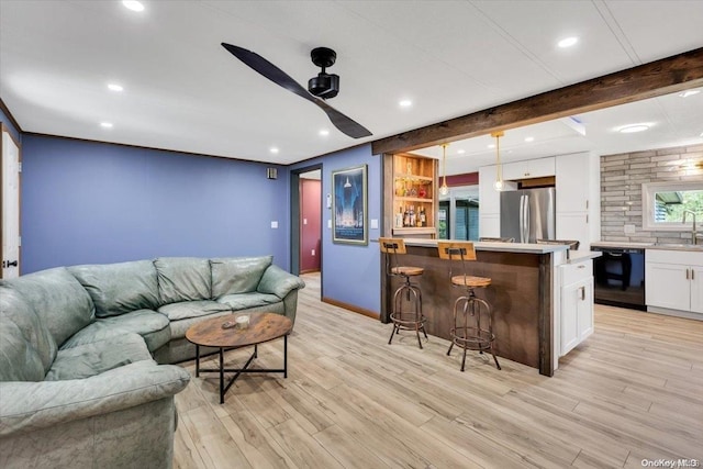 living room with ceiling fan, beam ceiling, sink, and light hardwood / wood-style flooring