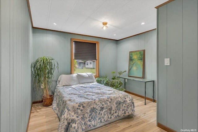 bedroom with light hardwood / wood-style floors, crown molding, and wooden walls